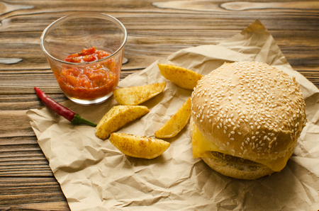 Cheeseburger with fried potatoes and chili  sauce on a  craft paper on wooden background with space for textの写真素材