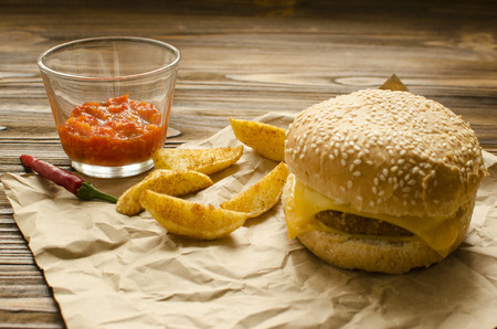 Cheeseburger with fried potatoes and chili  sauce on a  craft paper on wooden background with space for textの写真素材
