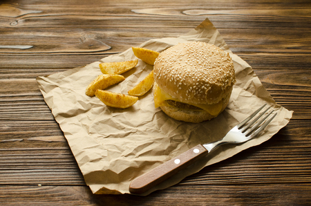 Cheeseburger with fried potatoes  in country style on a  craft paper on wooden background with space for textの写真素材