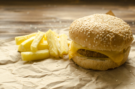 Cheeseburger with fried potatoes and chili on a  craft paper on wooden background with space for textの写真素材