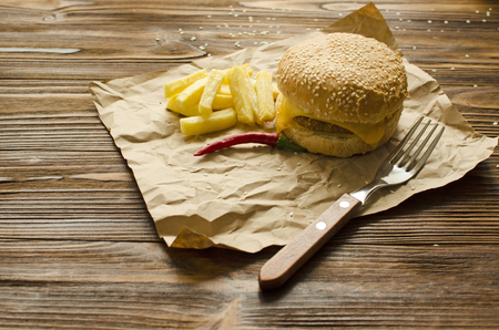 Cheeseburger with fried potatoes on a  craft paper on wooden background with space for textの写真素材