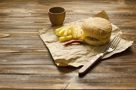 Cheeseburger with fried potatoes and chili  sauce on a  craft paper on wooden background with space for textの写真素材