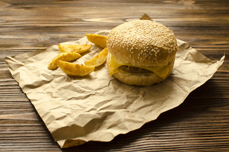 Cheeseburger with fried potatoes  in country style  on a  craft paper on wooden background with space for textの写真素材