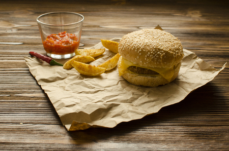 Cheeseburger with fried potatoes and chili  sauce on a  craft paper on wooden background with space for textの写真素材