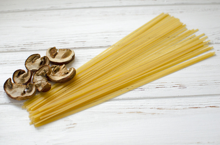 White dried mushrooms and pasta on wooden background ready for cookingの写真素材