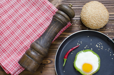 Fried egg in pepper on pan with chili pepper, sesame ban, pepper-caster on wooden backgroundの写真素材