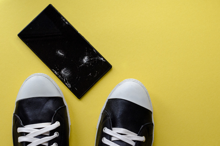 the foot in the sneakers steps on the phone on the yellow backgroungの写真素材