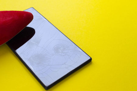 the foot in the red shoe steps on the phone on a yellow backgroundの写真素材