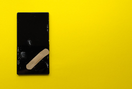 broken phone sticked plaster on yellow backgroundの写真素材