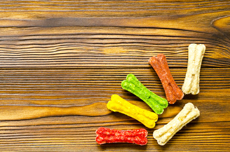 Delicious chewing colored bones for dogs with different tastes on wooden background with copy spaceの写真素材