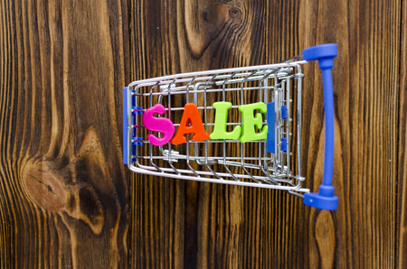 word "sale" and empty shopping cart on wooden backgroundの写真素材