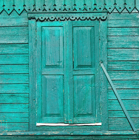 Old painted green wooden shuttered window on decorated wall.の写真素材