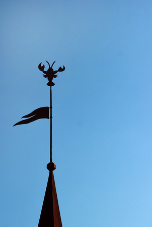 Silhouette of spire topped with flag and crab shaped weathercock.の写真素材