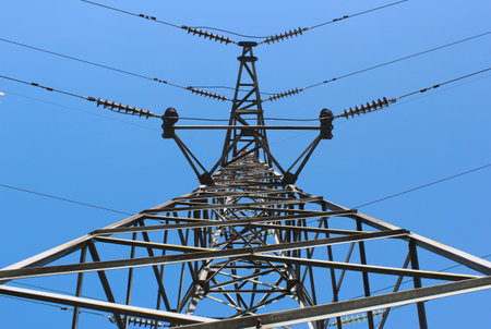High voltage post or power transmission line tower on blue sky background