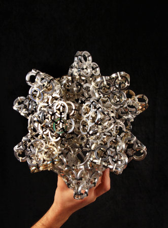 Hand holding artistic composition made of aluminum spacers concatenated with plastic zip ties...