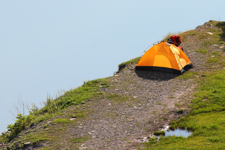Solitary orange tent camped near water edgeの写真素材