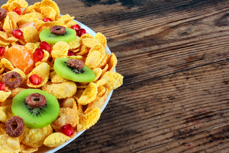 Corn flakes with kiwi and pomegranate on plate against old wooden table background.の写真素材