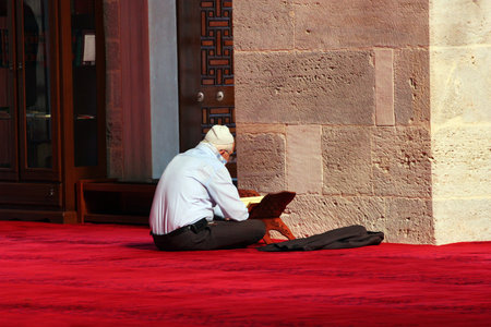 ISTANBUL, TURKEY - APRIL 7, 2012: Muslim man sitting on red carpet, reading Quran and praying at Mihrimah Sultan mosque in Istanbul.のeditorial素材
