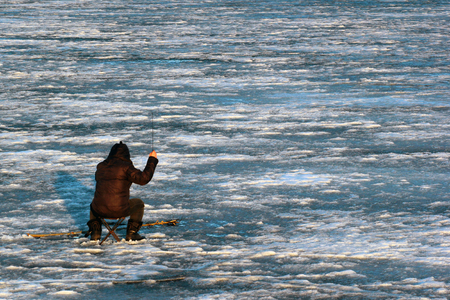 Lonely fisherman sitting on frozen iceの写真素材