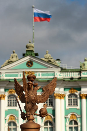 SAINT PETERSBURG, RUSSIA - JULY 5, 2017: Bronze double-headed eagle with sword, orb and cross. Symbol and coat of arms of Russia with Russian banner on Winter Palace.のeditorial素材