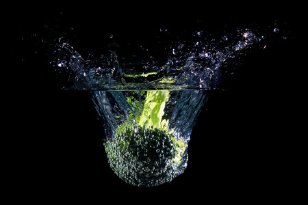 Broccoli falling into water, isolated against black backgroundの写真素材