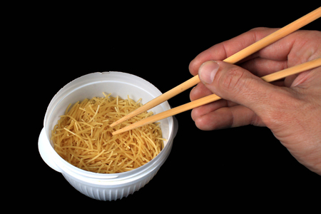 Hand holding chopsticks in a bowl of dry noodlesの写真素材