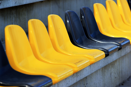 Row of old dirty plastic black and yellow seats at a stadiumの写真素材