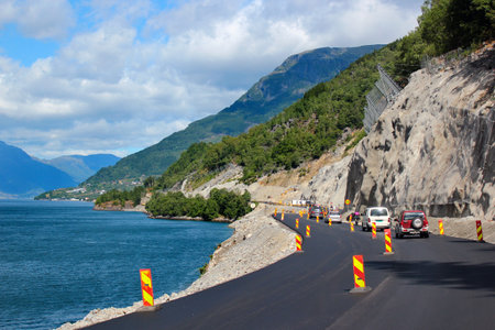 Ullensvang, Norway - June 22, 2018: New asphalt on a coastal road along Hardanger fjord. On the roadway being repaired traffic is controlled by road police.のeditorial素材