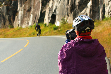 Biker photographer in raincoat and helmet takes picture of a cyclist on the roadの写真素材