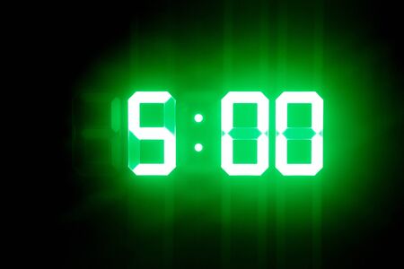 Green glowing digital clocks in the dark show 5:00 timeの写真素材
