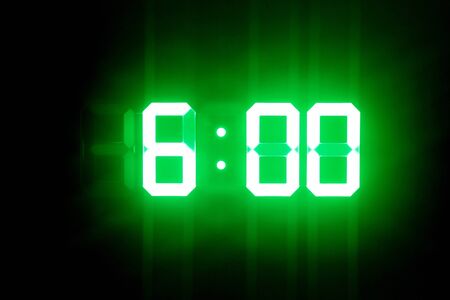 Green glowing digital clocks in the dark show 6:00 timeの写真素材
