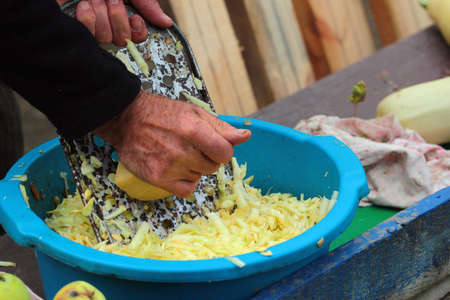 Man grates a squash. Hands hold grater and vegetable.の写真素材