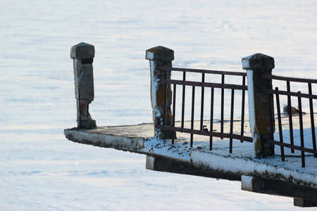 Detail of an old abandoned bridge with broken railing over a frozen riverの写真素材