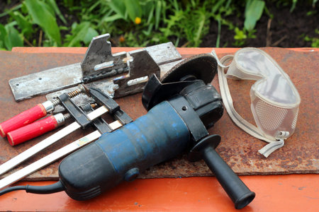 Angle grinder, safety goggles, f-clamps. Hand power tools, metalworking concept.