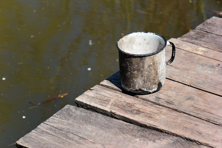 Old metal cup standing on a weathered wooden pier by the calm water