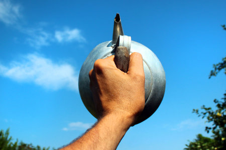 Hand holding metal kettle against blue skyの写真素材