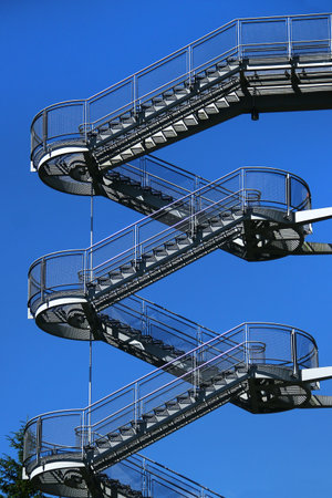 Exterior spiral staircase with metal mesh railings against clear blue skyの写真素材