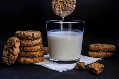 chocolate chip cookies are dipped in milk, on a black background, close-upの写真素材