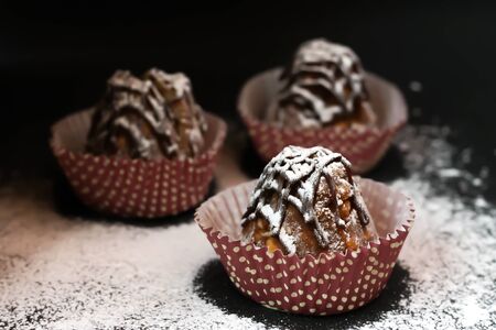 three anthill cakes in powdered sugar close-up, on a black backgroundの写真素材