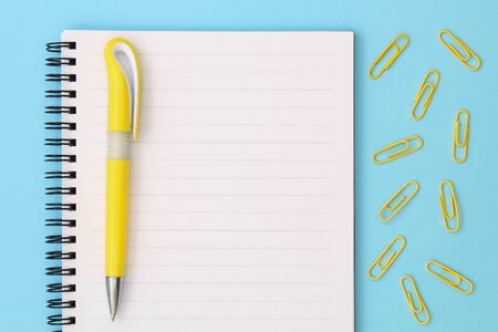 back to school creative concept. Notepad with yellow pen and clips on a blue background.の写真素材