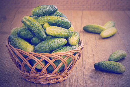 Green fresh cucumbers in a brown basket on a wooden tableの写真素材
