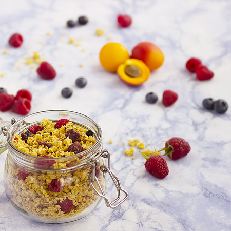 Bowls of  granola  with dry raspberries, cranberries and blueberries and fresh fruit on marble table. Soft focus.の写真素材
