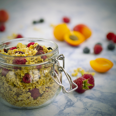 Bowls of  granola  with dry raspberries, cranberries and blueberries and fresh fruit on marble table. Soft focus.の写真素材