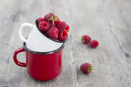Bright ripe raspberries in a metal cups on a gray wooden background. Soft focus.の写真素材