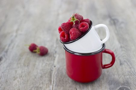 Bright ripe raspberries in a metal cups on a gray wooden background. Soft focus.の写真素材