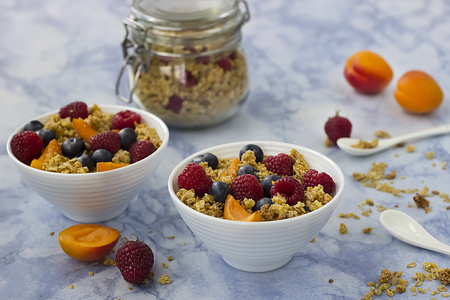Bowls of granola with blueberries and fresh fruit on marble table.の写真素材
