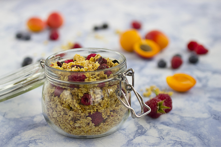 Bowls of  granola  with dry raspberries, cranberries and blueberries and fresh fruit on marble table. Soft focus.の写真素材