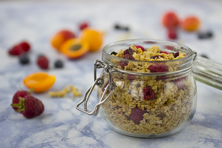 Bowls of  granola  with dry raspberries, cranberries and blueberries and fresh fruit on marble table. Soft focus.の写真素材