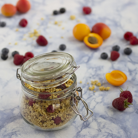 Bowls of  granola  with dry raspberries, cranberries and blueberries and fresh fruit on marble table. Soft focus.の写真素材