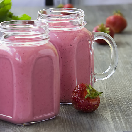 Strawberry smoothies in a glass bottle, mint leaves and whole strawberry berries on a gray wooden background. The concept of diet, fitness and healthy eating. Soft focus. Square.の写真素材